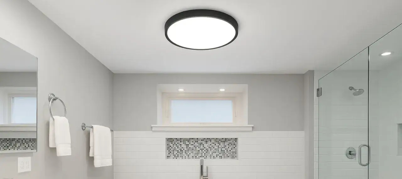 Salle de bain moderne avec plafonnier rond noir. Id&eacute;al pour changer ampoule plafonnier hublot. Douche vitr&eacute;e, lavabo et serviettes blanches.