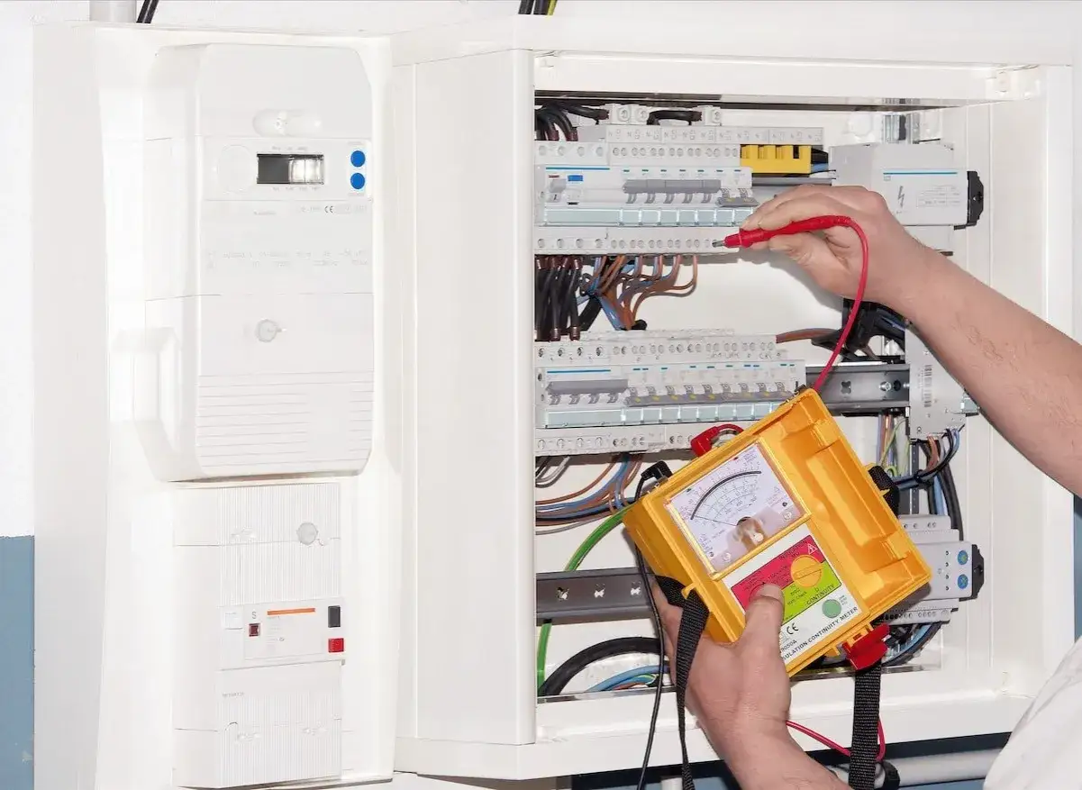 Un électricien vérifie un tableau électrique, peut-être pour déterminer si l'installation est monophasé ou triphasé, à l'aide d'un testeur.