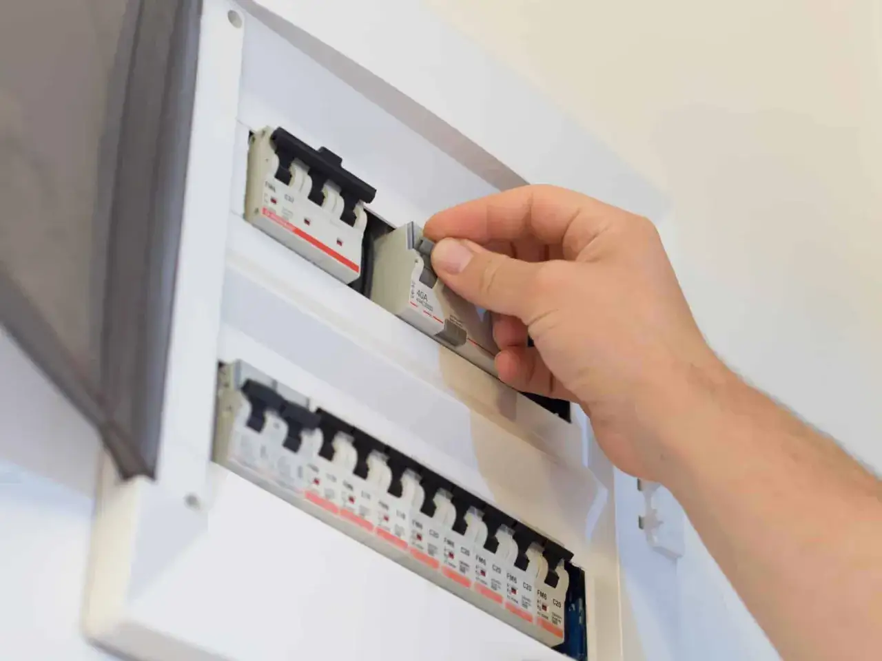 Main d'un électricien manipulant un disjoncteur d'abonné dans un tableau électrique.