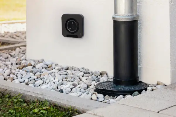 Une prise femelle étanche noire est fixée au mur blanc, à côté d'une descente d'eau.